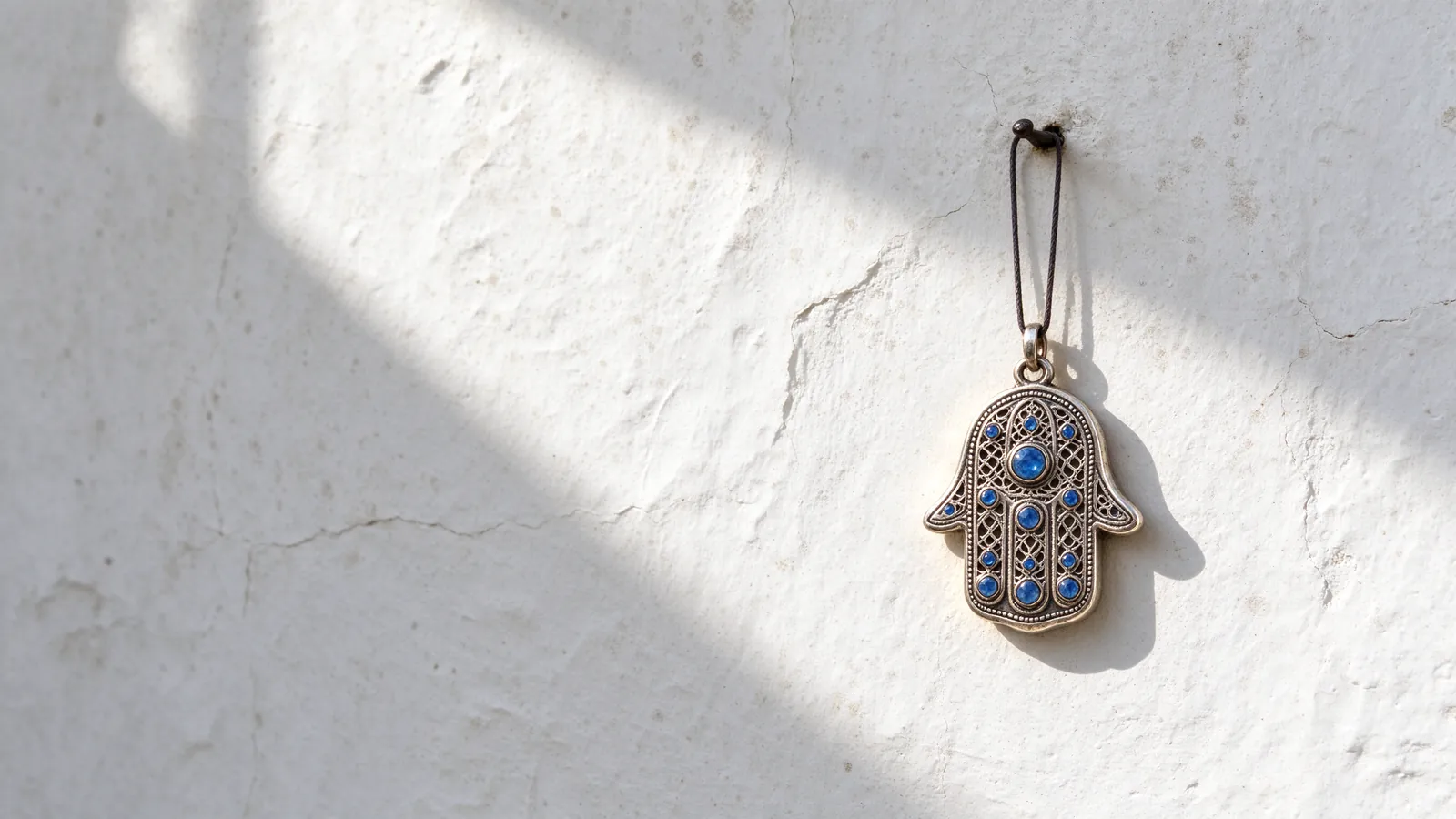 Main de Fatma (hamsa) en argent ornée de pierres bleues sur un mur blanc