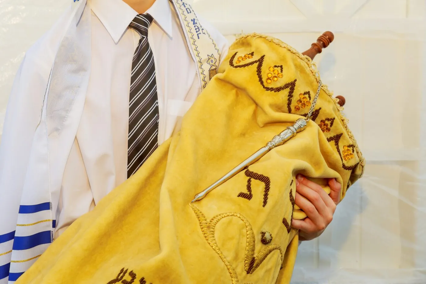 Jeune homme en talith portant un rouleau de la Torah recouvert d'un manteau de velours jaune brodé, avec son yad en argent