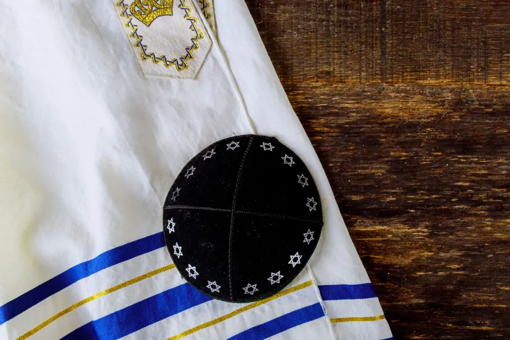 Kippa noire brodée posée sur un talith blanc à rayures bleues