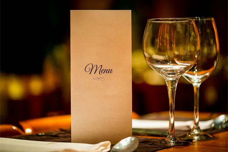 Carte de menu posée sur une table dressée avec des verres à pied, avant une réception