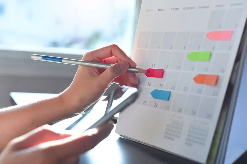 Parent notant les étapes de l’organisation d’une Bar Mitzvah sur un calendrier mural couvert de marque-pages de couleur