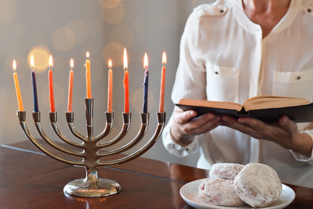 Woman reading Chanukah blessings in Torah book with Menorah lit with nine candles in front of her